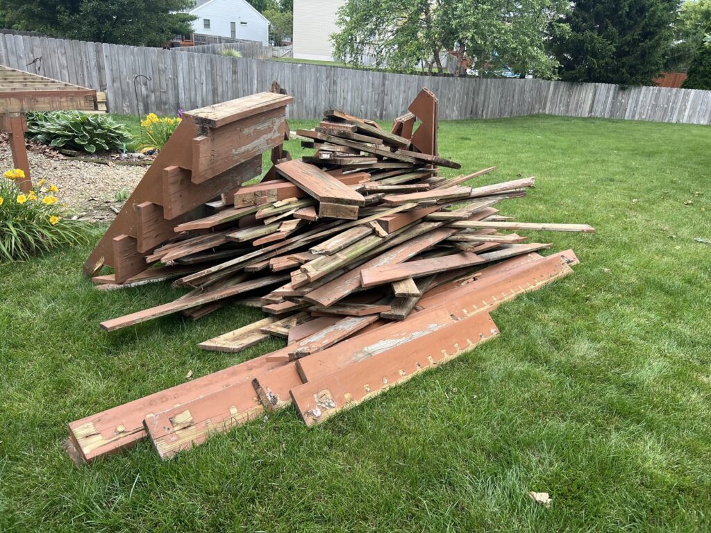 A pile of old, painted wooden deck boards on a green lawn, ready for general junk removal by Top Tier Waste Services LLC in Lancaster, OH
