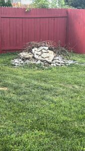 A pile of rocks and yard debris in a grassy backyard, ready for removal by Dumpin' Junk in Martinsburg, WV.