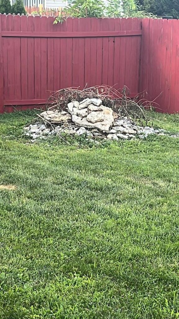 A pile of rocks and yard debris in a grassy backyard, ready for removal by Dumpin' Junk in Martinsburg, WV.