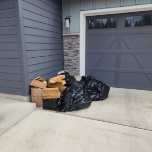 A pile of black trash bags and wooden debris stacked outside a garage, awaiting pickup by Junk Management in Vancouver, WA.