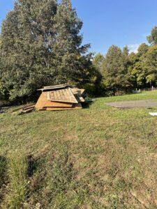 A pile of wooden planks and construction debris in a grassy area, awaiting removal by DC'S Removal Service in Neelyville, MO.