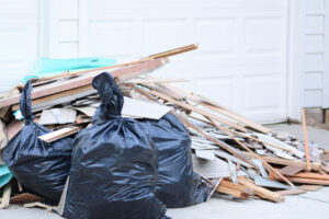 Black trash bags and a pile of wood scraps and debris in front of a garage, indicating a junk removal service by Dumpster 360 in Clarksville, TN.