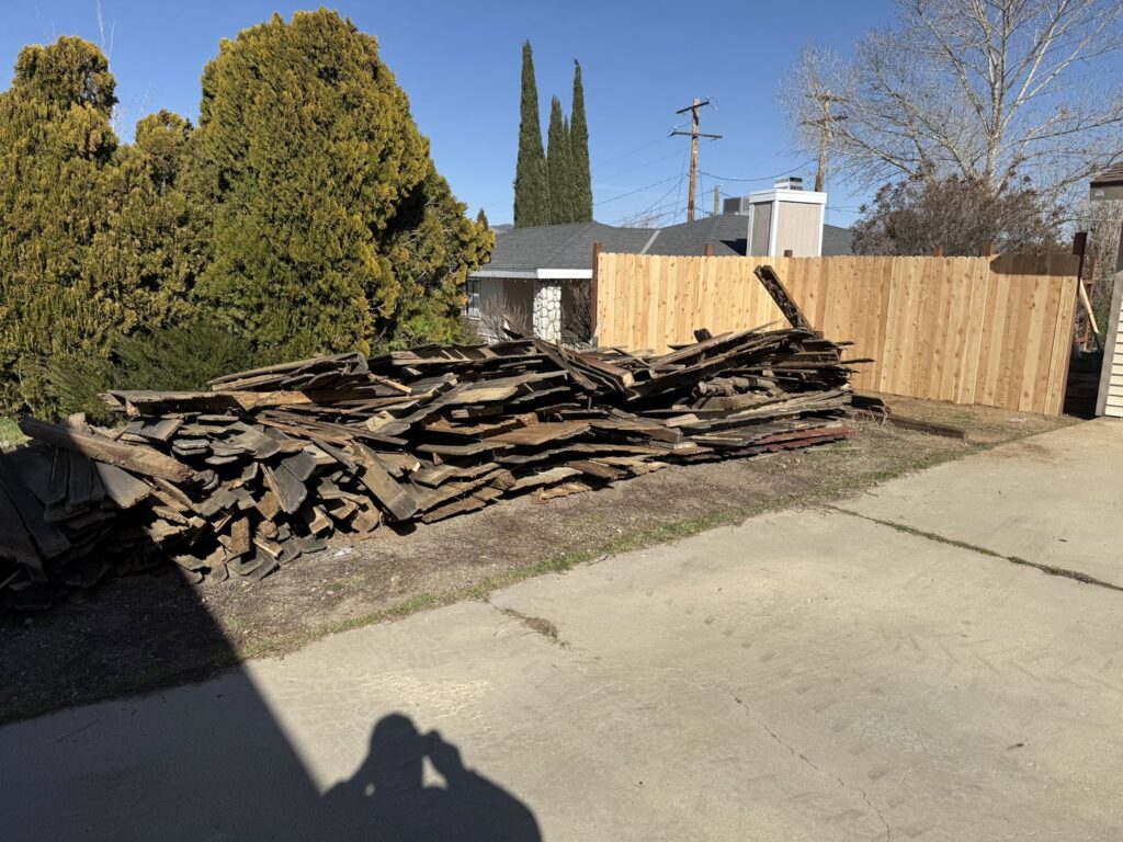 A large pile of old wooden debris in a residential yard, ready for removal by Kern County Junk Removal in Bakersfield, CA.