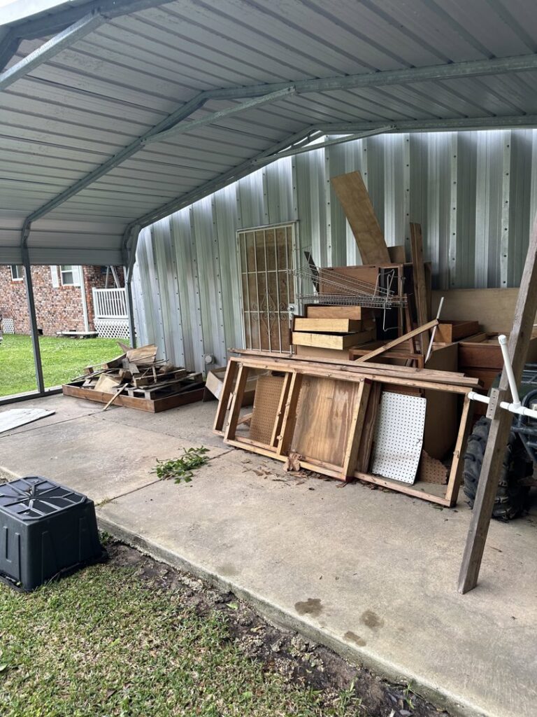 A pile of wooden debris, shelves, and other junk under a carport, awaiting removal by Clutter Control Junk Removal and Demo in Biloxi, MS.