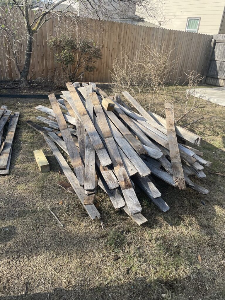 A large pile of old wooden planks and debris on the grass, ready for junk removal by Silverhull Junk Removal in San Antonio, TX