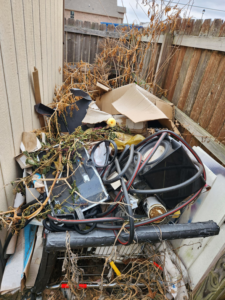 A pile of yard debris, cardboard, and miscellaneous junk items by a fence, ready for removal by Urban Junk Removal, LLC in Springdale, AR.