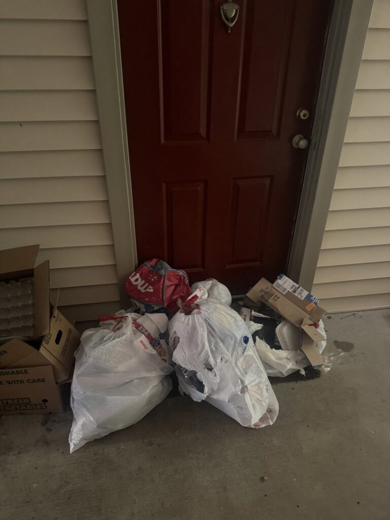 Multiple trash bags and cardboard boxes piled up next to a red door, ready for junk removal by A1 Valet Trash in Atlanta, GA.