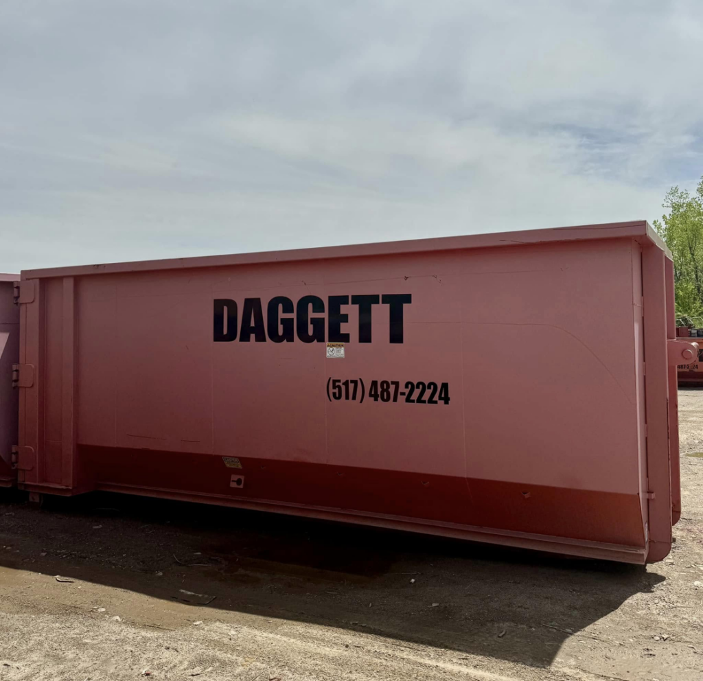 A large pink dumpster with 'DAGGETT' branding from Daggett Container Service LLC, available for junk removal in Lansing, MI.