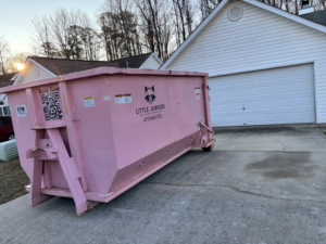 A pink dumpster from Little Junkers placed in a residential driveway for junk removal in Peachtree City, GA.
