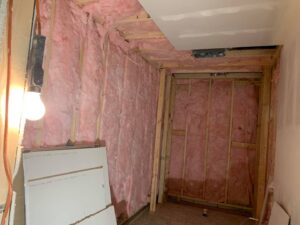 Pink insulation installed between wall studs in a room, a home improvement service by Vazquez Quality Construction Inc in Aurora, CO.