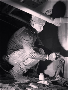 A plumber repairing pipes in a confined crawlspace or basement with a wrench for Sandobros Plumbing in Charleston, SC