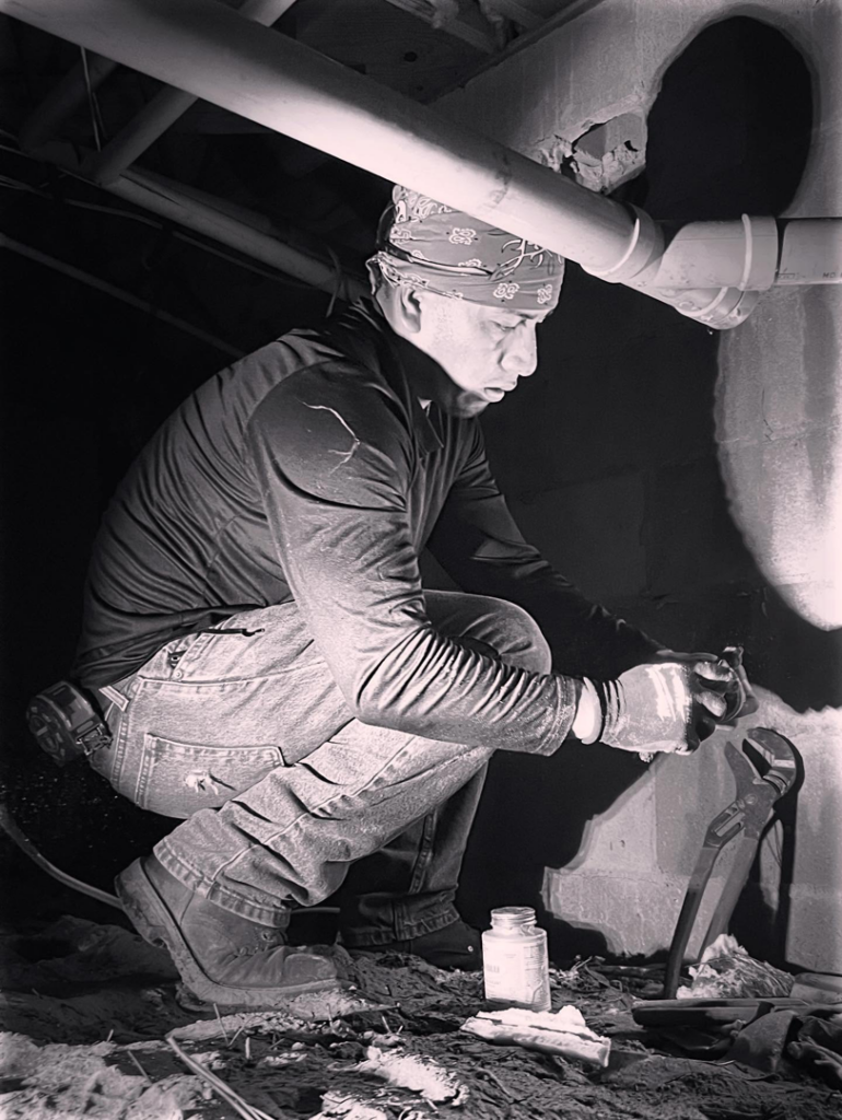 A plumber repairing pipes in a confined crawlspace or basement with a wrench for Sandobros Plumbing in Charleston, SC