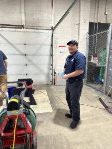 A plumber standing next to a drain cleaning machine, ready for service, from Top-Notch Plumbing, Heating & Air in Greeley, CO.