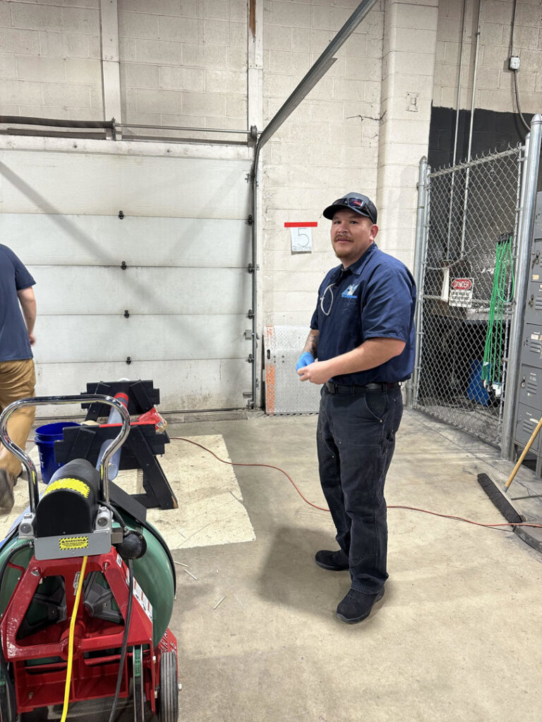 A plumber standing next to a drain cleaning machine, ready for service, from Top-Notch Plumbing, Heating & Air in Greeley, CO.