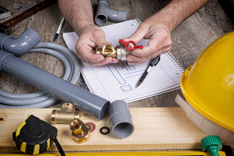 A handyman working on plumbing repair with pipes and a valve at Nail Builders, Inc. in Littleton, CO