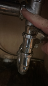 A hand pointing to a connection on a chrome sink drain pipe, indicating plumbing repair by Katzenstein llc handyman in Council Bluffs, IA.