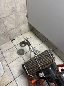 A plumbing snake and tools on a tiled bathroom floor, ready for drain cleaning services by Byrd Property Restoration, LLC in Parkersburg, WV.
