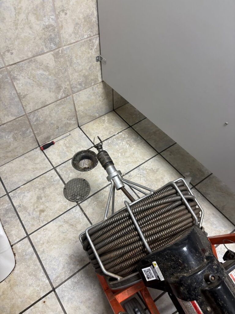 A plumbing snake and tools on a tiled bathroom floor, ready for drain cleaning services by Byrd Property Restoration, LLC in Parkersburg, WV.