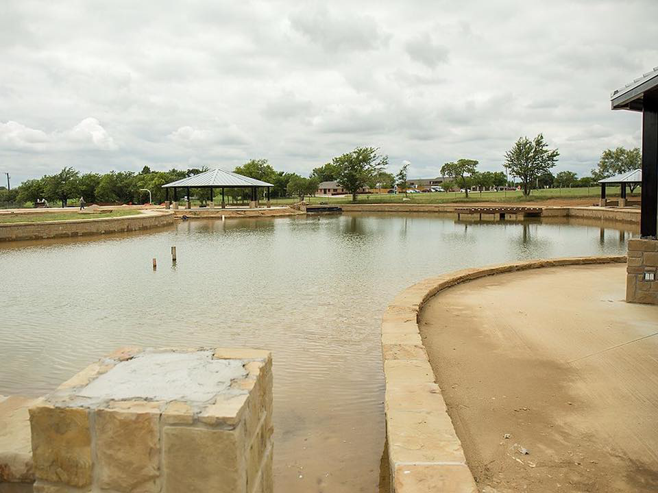 A pond with stone edging and concrete structures, part of a park development by Northstar Construction, LLC in Fort Worth, TX
