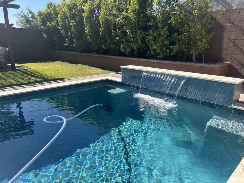 A clean swimming pool with a waterfall feature and a pool cleaner, showcasing pool cleaning service by Fair & Square Pools in Chandler, AZ