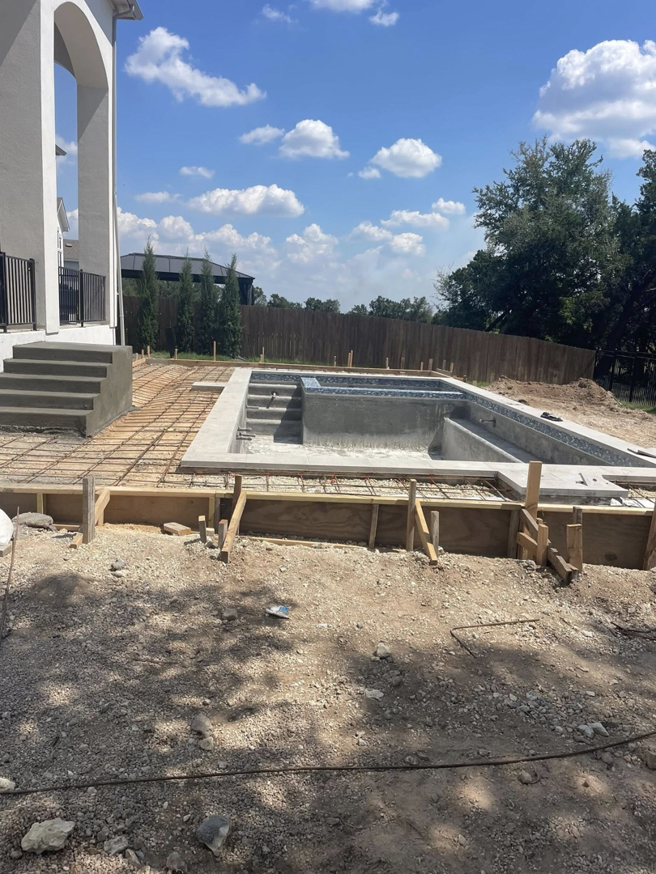 A pool construction site showing the pool shell, rebar, and wooden forms for decking by Austin Pool Plastering in Austin, TX.
