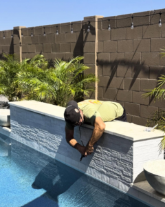 A pool maintenance worker performing a handyman job on a tiled pool wall at Fair & Square Pools in Chandler, AZ