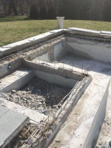 An empty swimming pool undergoing renovation with visible rebar and construction debris, handled by B-rod Pool Service LLC in Norwalk, CT.