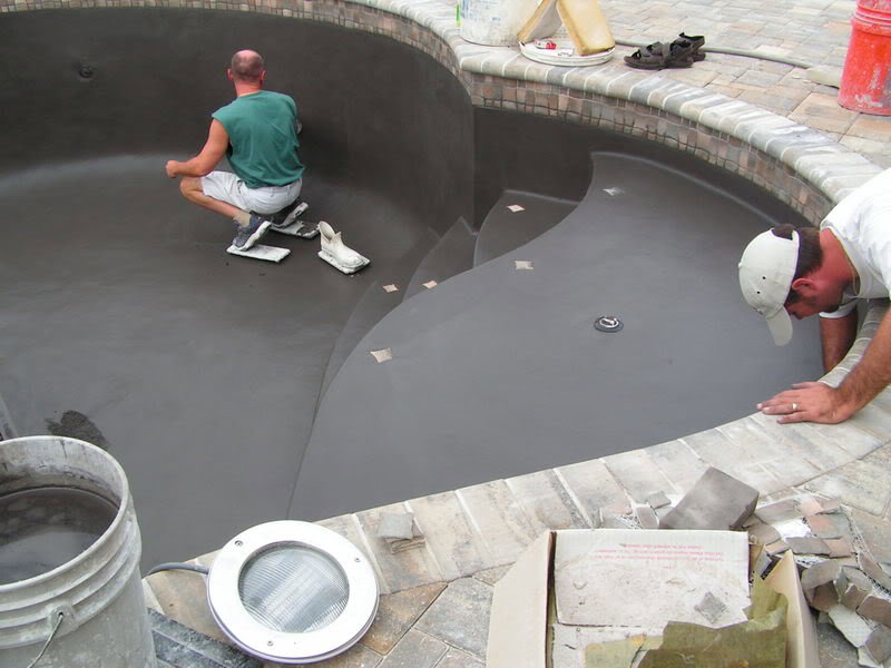 Two workers applying a new surface coating inside an empty swimming pool, a service by B-rod Pool Service LLC in Norwalk, CT.