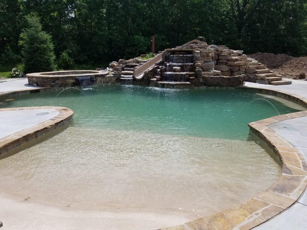 Custom pool featuring a rock waterfall, slide, and beach entry by Elevate Pools in O'Fallon, MO.