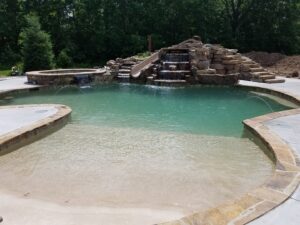 Custom pool featuring a rock waterfall, slide, and beach entry by Elevate Pools in O'Fallon, MO.
