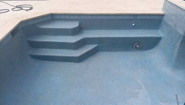 Close-up of pool steps with a new plaster finish and blue tile accents by Austin Pool Plastering in Austin, TX.