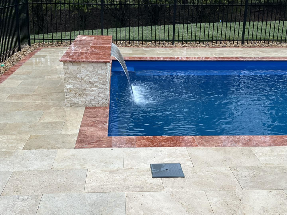 A beautiful pool waterfall feature with natural stone patio installed by Southern Pool Solutions in Knoxville, TN.