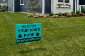 A 'We Scoop Your Dogs Poop' sign displayed on a green lawn, indicating pet waste removal services by They Poop We Scoop in Lewes, DE.