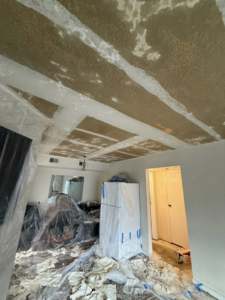 A room undergoing popcorn ceiling removal with covered furniture and debris on the floor by AM Remodels LLC in Denver, CO.