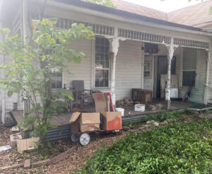 An old house porch cluttered with boxes and various items, indicating a junk removal job for G.I. HAUL Austin, TX.