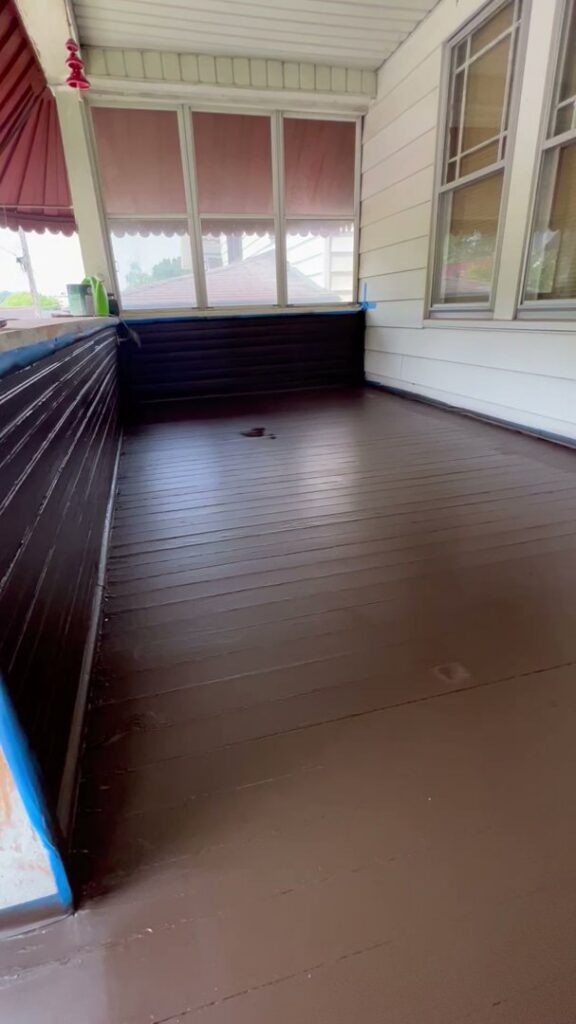 A porch floor and lower walls freshly painted dark brown, with painter's tape visible, showing work in progress by OG Renovations in Huntington, WV.