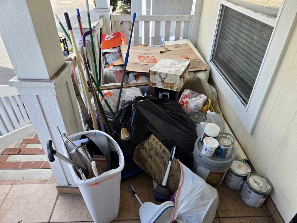 A porch overflowing with household junk, trash bags, and paint cans, ready for removal by Titan Junk Co. in San Diego, CA