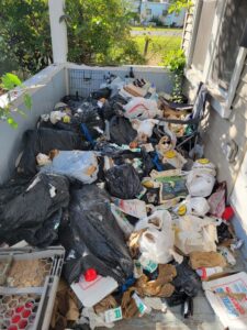 A porch completely overflowing with trash bags and loose debris, indicating a significant junk removal job for Rizzo Junk Removal in Nashua, NH.