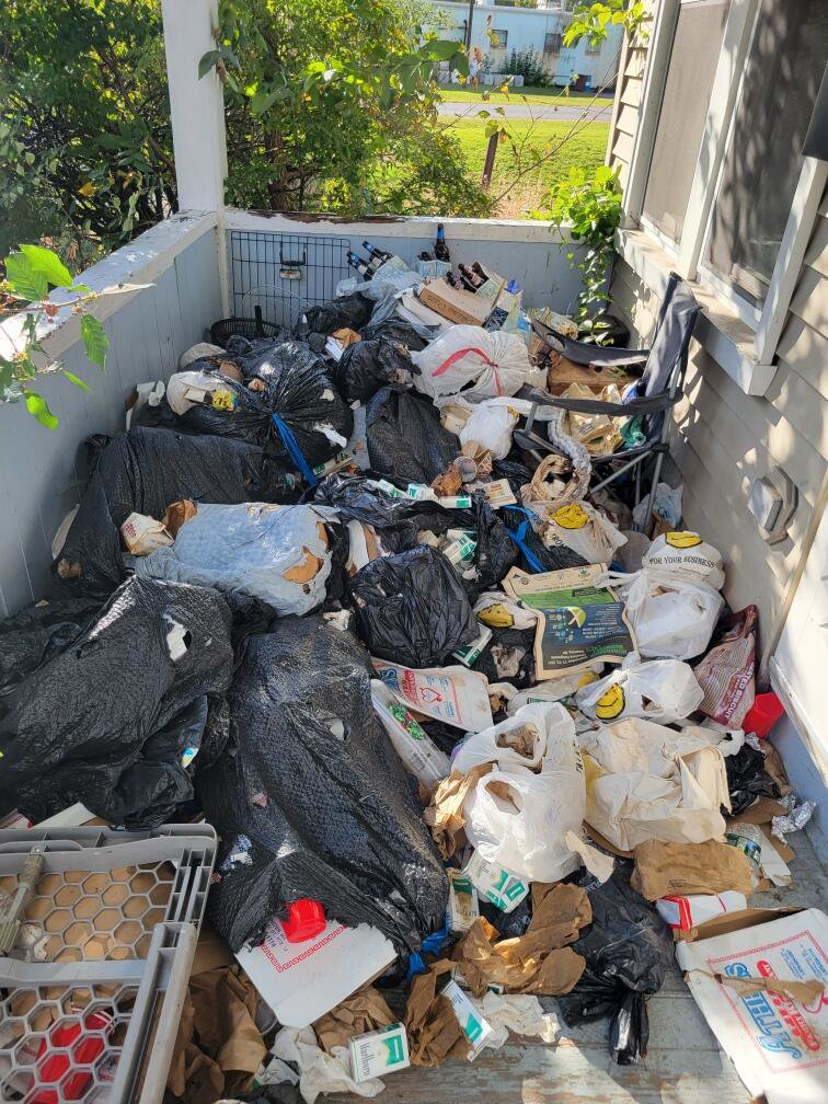 A porch completely overflowing with trash bags and loose debris, indicating a significant junk removal job for Rizzo Junk Removal in Nashua, NH.