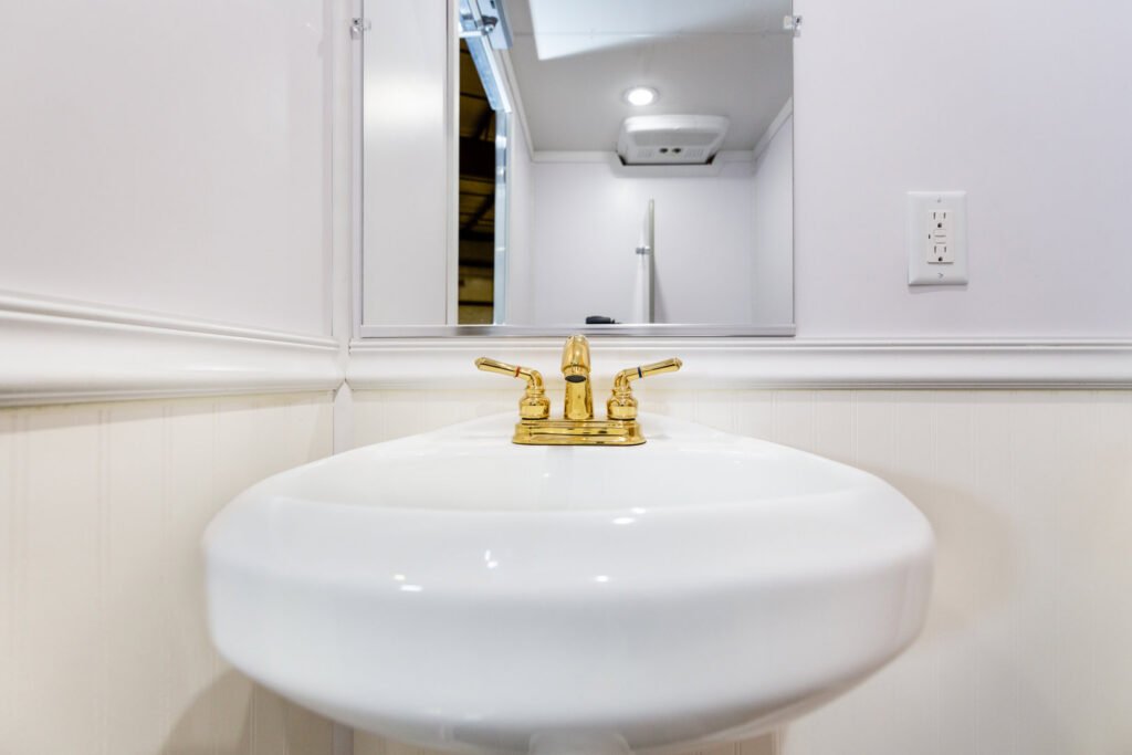 Interior of a portable restroom showing a modern sink and mirror by Comforts of Home Services Inc in Aurora, IL.