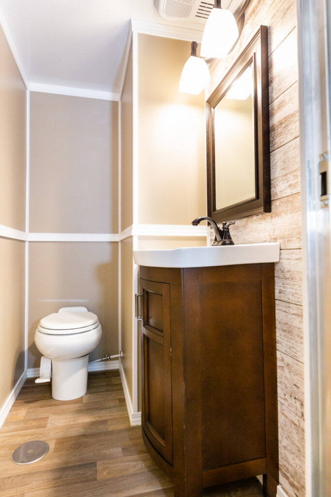 Interior of a portable restroom showing a toilet and dark wood vanity by Comforts of Home Services Inc in Aurora, IL.