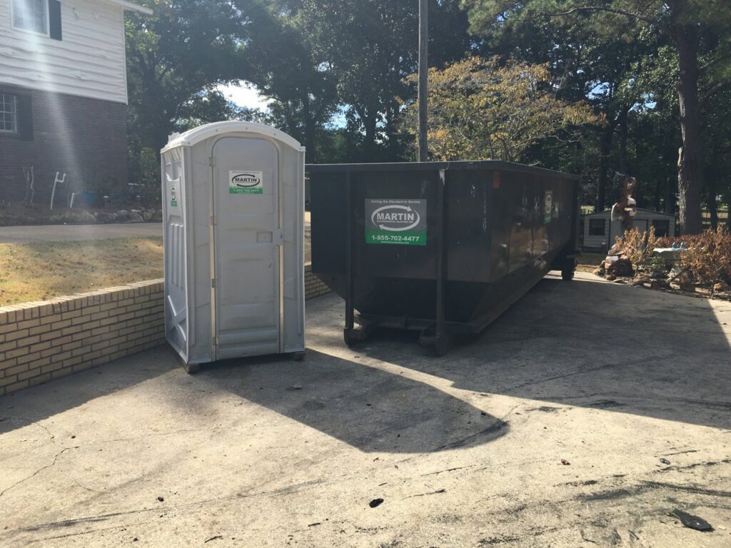 A portable toilet and a large roll-off dumpster from Martin Environmental on a driveway in Dothan, AL.