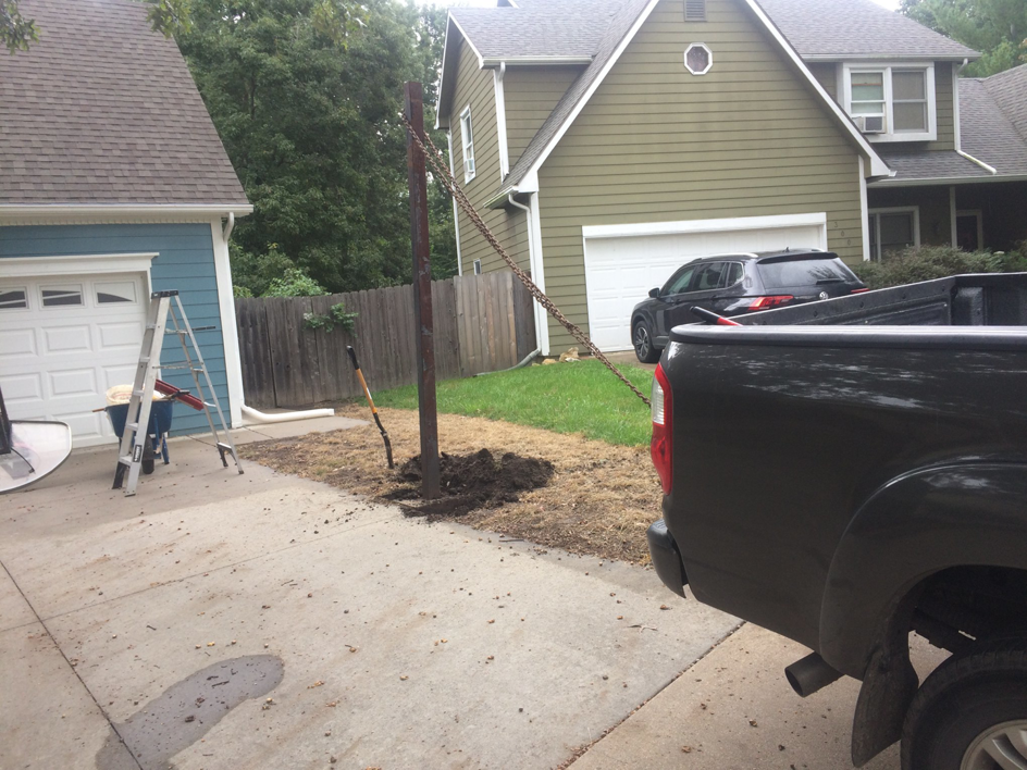 A handyman installing a post in a backyard, with tools and a ladder nearby, by The Hot Handyman in Lawrence, KS.