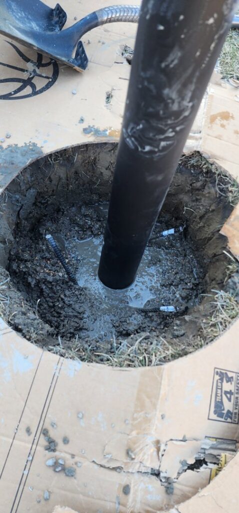 A wooden post being set into a concrete foundation in a dug hole by SAM'S Handywork LLC in Independence, IA.