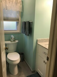 A freshly renovated powder room with light green walls, a new vanity, and toilet, completed by Pink Rose Home Service in Rochester, NY.