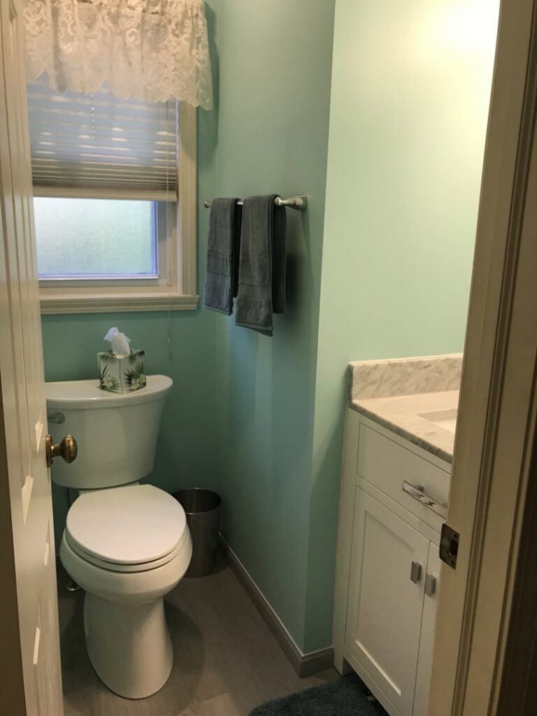 A freshly renovated powder room with light green walls, a new vanity, and toilet, completed by Pink Rose Home Service in Rochester, NY.