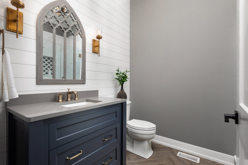 A stylish powder room with a dark blue vanity, shiplap wall, and unique mirror, completed by Autumn Homes in Naperville, IL.
