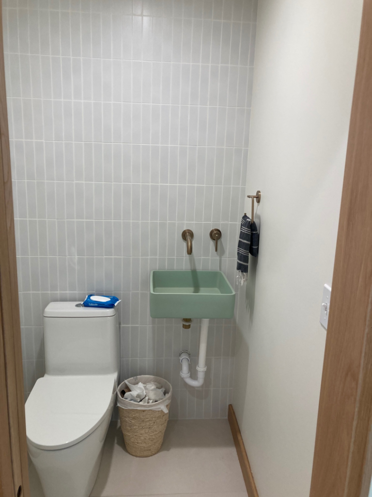 A small powder room with light grey subway tiles and a unique green wall-mounted sink installed by Tess Tile By Design in Kansas City, MO.