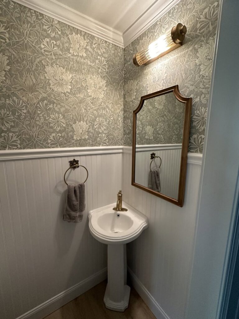A beautifully renovated powder room with a pedestal sink and decorative wallpaper by Stanley Contracting in Whiting, NJ