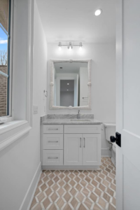 A stylish powder room featuring a white vanity, decorative mirror, and patterned floor tiles installed by CML Builders in Charlotte, NC.